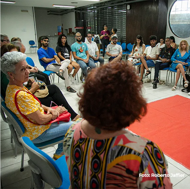 Roda de conversa vista de cima, cadeiras em círculo sobre tapete vermelho