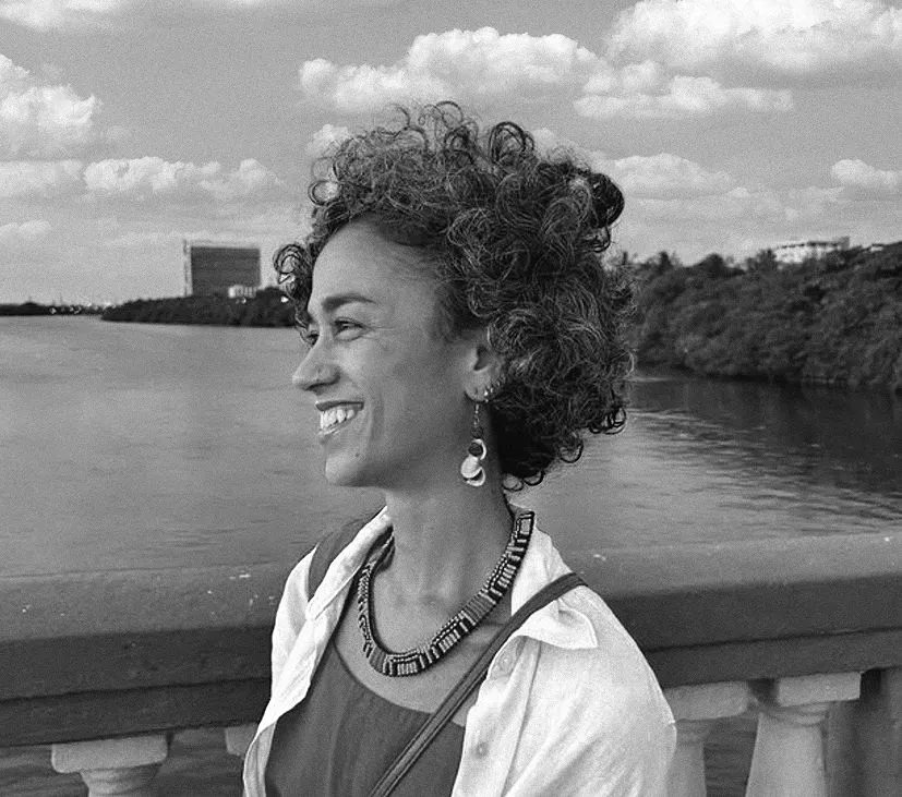 Jessica Lobo sorrindo, de perfil, à beira do rio
