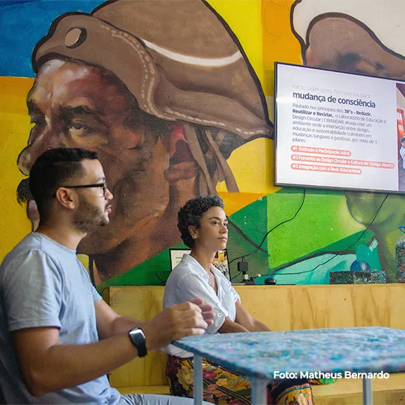 Duas pessoas conversam diante de um mural colorido durante a oficina