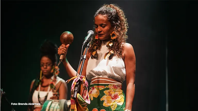 Cantoras se apresentam no palco com maracás