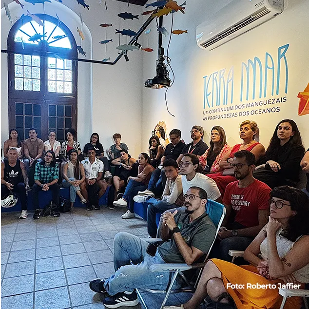 Plateia reunida na exposição, sob esculturas suspensas