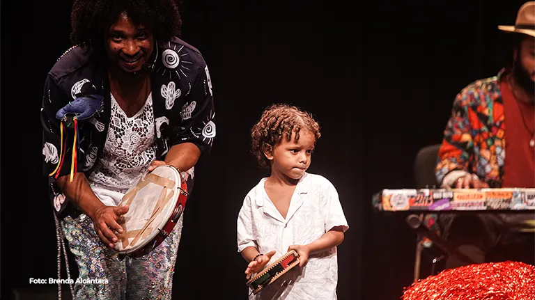 Músico e criança tocam percussão juntos no palco